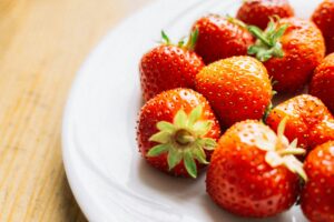 Close-up of fresh strawberries on a white plate with wooden background.